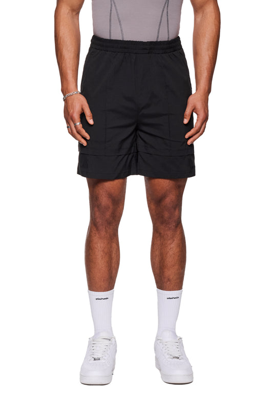 Mann trägt Track Shorts Black mit elastischem Bund und Kordelzug, kombiniert mit weißen Sneakers und Socken. Perfekt für Alltag und vielseitig einsetzbar.