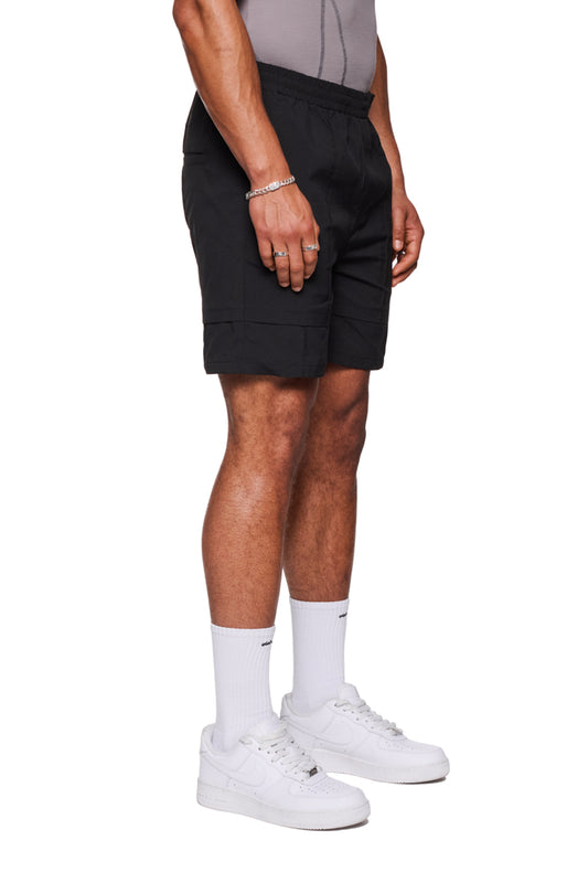 Ein Mann trägt schwarze Track Shorts mit elastischem Bund und gesticktem OLAKALA-Logo, perfekt für Alltag und vielseitig als Badehose einsetzbar.