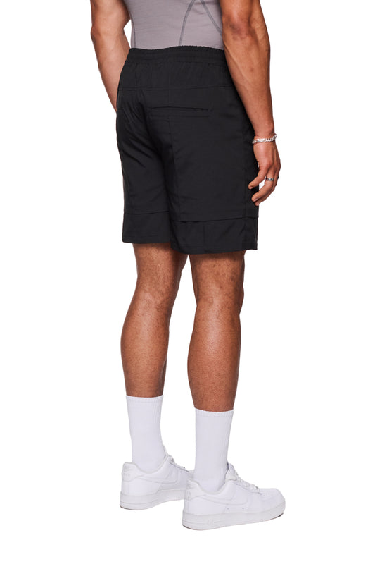 Person trägt schwarze Track Shorts mit elastischem Bund und französischen Taschen, kombiniert mit weißen Sneakers. Ideal für Alltag und als Badehose.