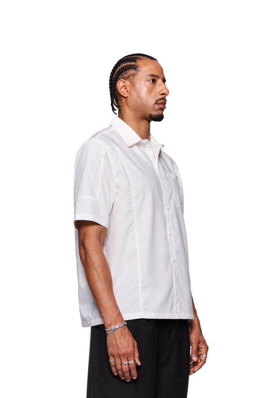 Man with braids wears the CC short sleeve shirt white by OLAKALA, loose fit, with logo embroidery and button placket.
