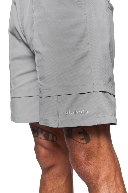 Person trägt Track Shorts Gray mit elastischem Bund und französischen Taschen, ideal für Alltag und Badespaß. Robustes, wasserabweisendes Gewebe, OLAKALA Logo sichtbar.