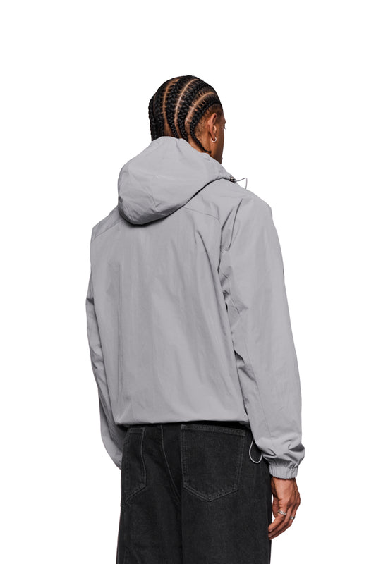 Man wears gray windbreaker with hood and embroidered OLAKALA logo on the chest. Jacket has zippered pockets and elastic cuffs. Unisex and windproof.