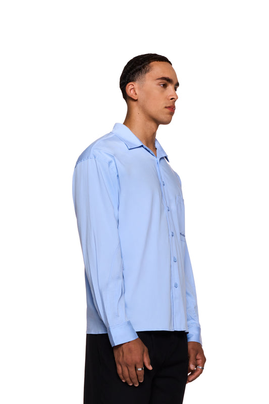 Mann trägt das CC Anatomy Shirt Blue mit Knopfleiste, doppeltem Kragen, Brusttasche und OLAKALA-Logo. Lockerer Schnitt, unisex Design.