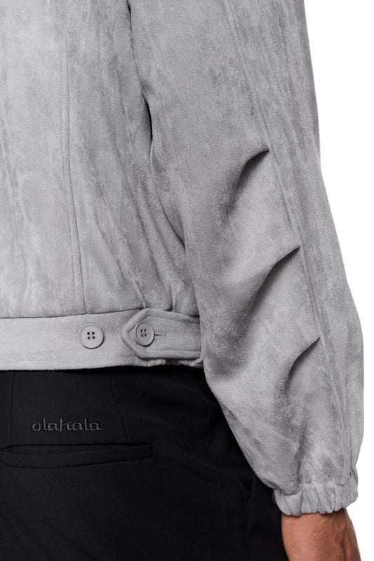 Nahaufnahme der CC Anatomy Velour Jacket Light Gray mit doppeltem Kragen, asymmetrischem Rücken und paspelierten Taschen, getragen von einer Person.