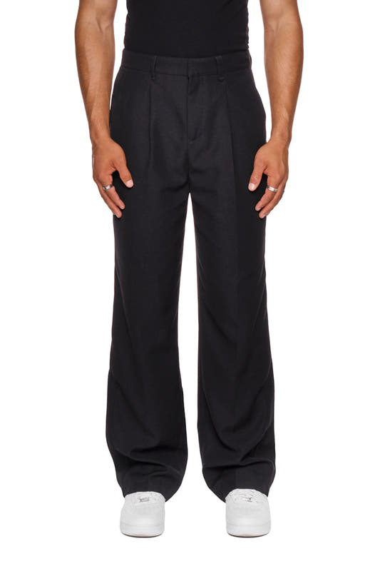 Man wears CC Dress Pants Regular Black with French pockets, pleats and embroidered OLAKALA logo, emphasizing soft, robust twill fabric.