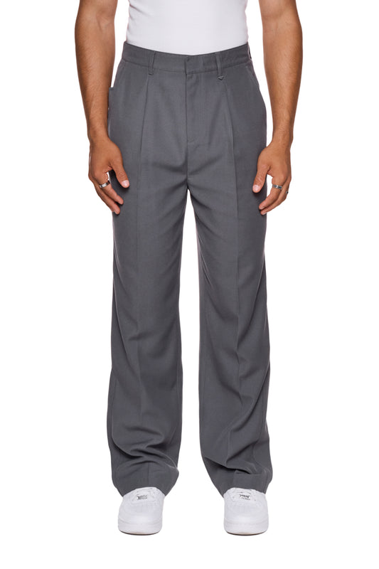 Mann trägt CC Dress Pants Regular Gray mit französischen Taschen und gesticktem OLAKALA Logo über der rechten Gesäßtasche, stehend auf weißem Untergrund.