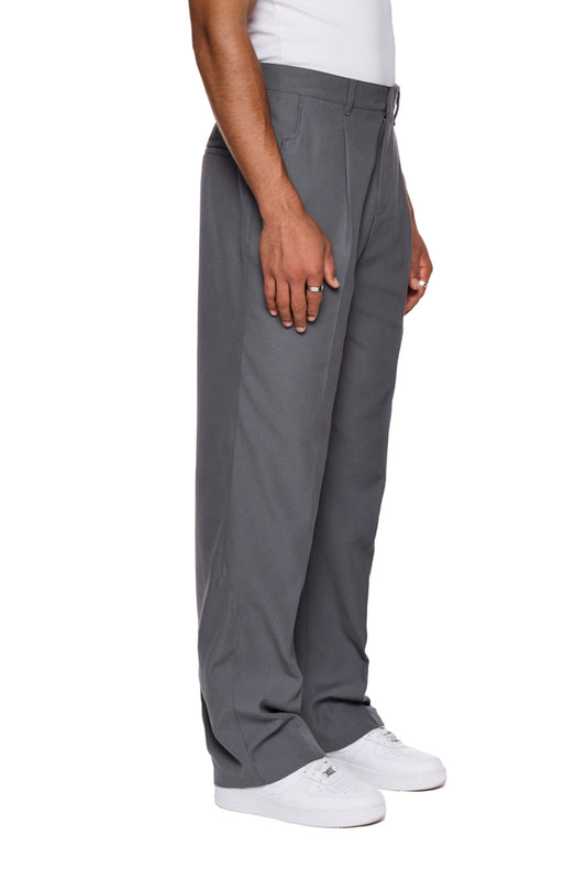 Person trägt CC Dress Pants Regular Gray mit französischen Taschen und Paspeltaschen, zeigt gesticktes OLAKALA Logo über rechter Gesäßtasche.