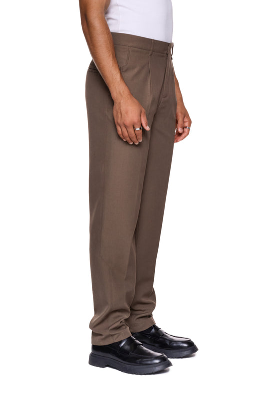 Person trägt CC Dress Pants Slim Fit Brown mit französischen Taschen, asymmetrischem Eingriff und gesticktem OLAKALA Logo über der rechten Gesäßtasche.