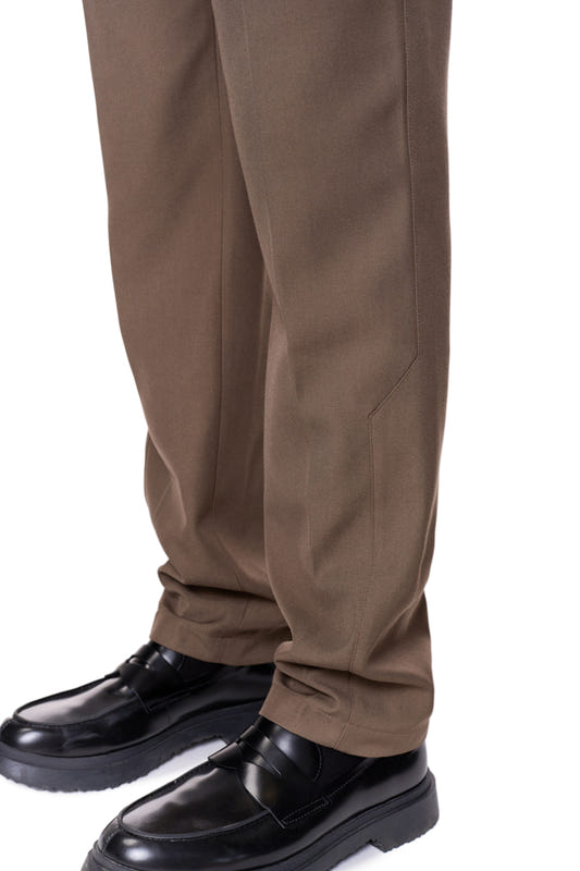 Leg view in CC Dress Pants Slim Fit Brown, with asymmetrical pocket and embroidered OLAKALA logo, emphasizes the slim fit and pleats.