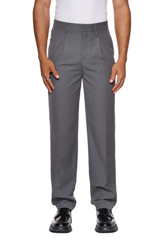 Mann trägt CC Dress Pants Slim Fit Gray mit asymmetrischer Tasche, Bundfalten und gesticktem OLAKALA-Logo über der rechten Gesäßtasche. Schmale Passform, robustes Köper-Gewebe.
