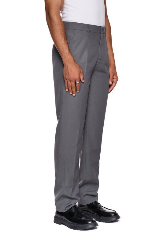 Mann trägt CC Dress Pants Slim Fit in Grau mit asymmetrischen Taschen und OLAKALA Logo auf Gesäßtasche, zeigt elegantes Design und schmale Passform.
