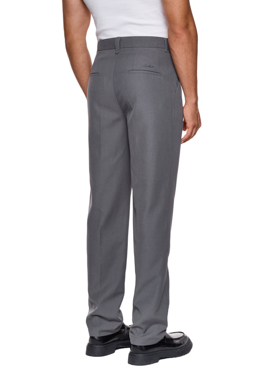 Person trägt CC Dress Pants Slim Fit Grau mit französischen Taschen, asymmetrischem Eingriff und gesticktem OLAKALA-Logo über der rechten Gesäßtasche, zeigt schmale Passform.