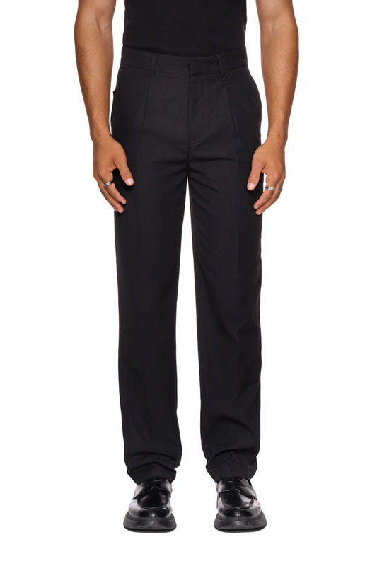 Mann trägt CC Dress Pants Slim Fit Black mit asymmetrischen Taschen und gesticktem OLAKALA Logo, schmale Passform, betont durch Bundfalten und versetzte Seitennaht.