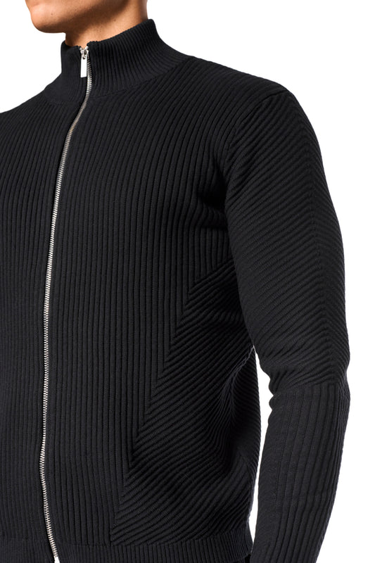 Mann trägt CI Slim Knit Jacket in Schwarz mit Reißverschluss vorne, schmaler Passform und verschiedenen Strickmustern. Unisex-Design von OLAKALA.