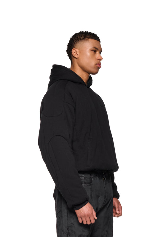 Mann trägt einen gepufften Greyzone Puffer Hoodie mit gesticktem OLAKALA-Logo, Ripp-Bündchen und elastischem Saum.