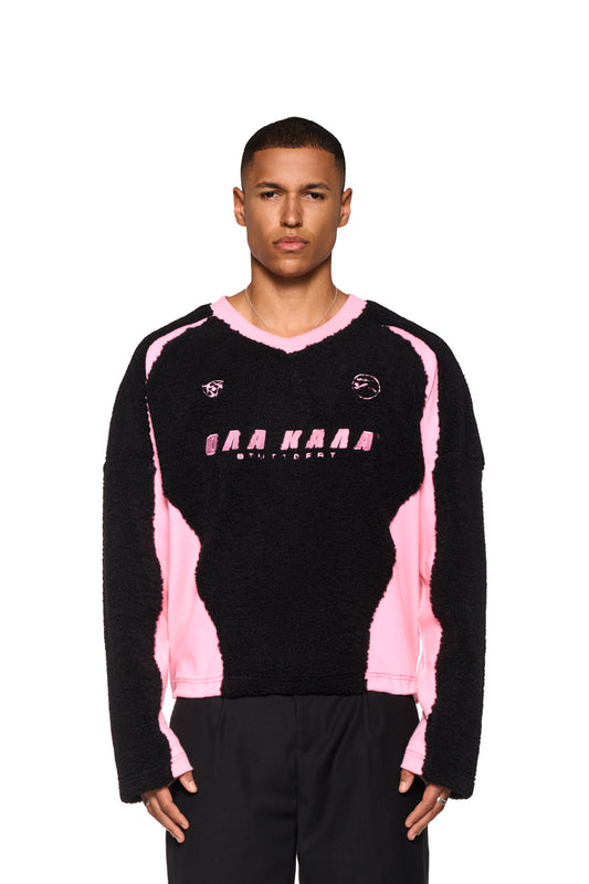 Mann trägt Fleece V-Ausschnitt Pullover Pink mit gesticktem OLAKALA Logo und Icons, oversized Passform, unisex, verstellbarer Saum.