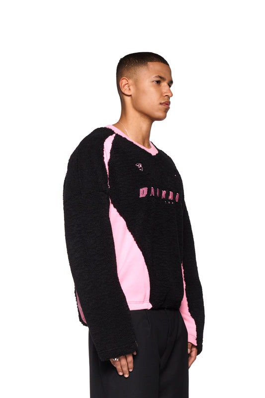 Mann trägt Fleece V-Neck Sweater Pink mit gesticktem OLAKALA Logo und Icons, oversized Passform.
