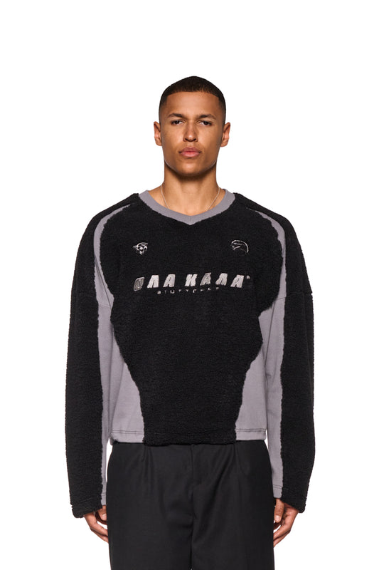 Mann trägt schwarzen Fleece V-Neck Sweater mit gesticktem OLAKALA Stuttgart Logo und Icons, elastischer Saum durch Kordelzüge, oversized Unisex-Passform.