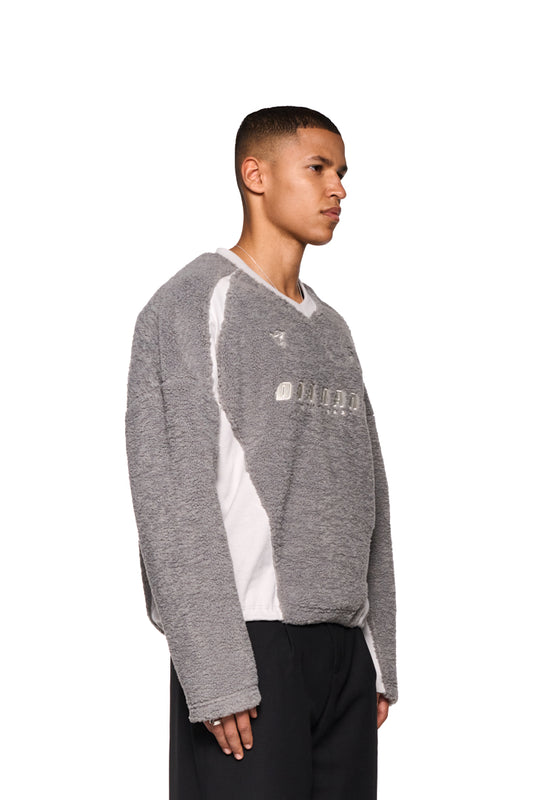 Mann trägt grauen Fleece-V-Ausschnitt-Pullover mit gesticktem OLAKALA Stuttgart-Logo und Isolation Jersey-Icon. Oversized, unisex, verstellbarer elastischer Saum.