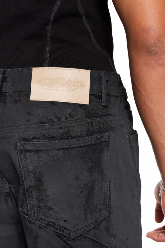 CI Coated Denim Pants Regular mit „Destroyed-Allover-Print“, 5-Pocket-Design, geprägtem OLAKALA-Patch am Bund und versetzter Seitennaht, getragen von einer Person.