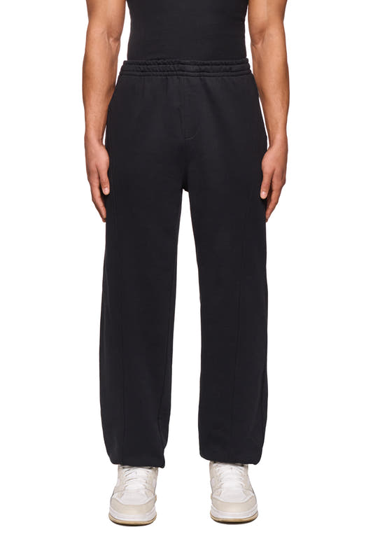 Person wears CC Core Sweatpants Black with elastic waistband and drawstring, ribbed cuffs and dividing seams for an elegant look. Unisex, durable material.