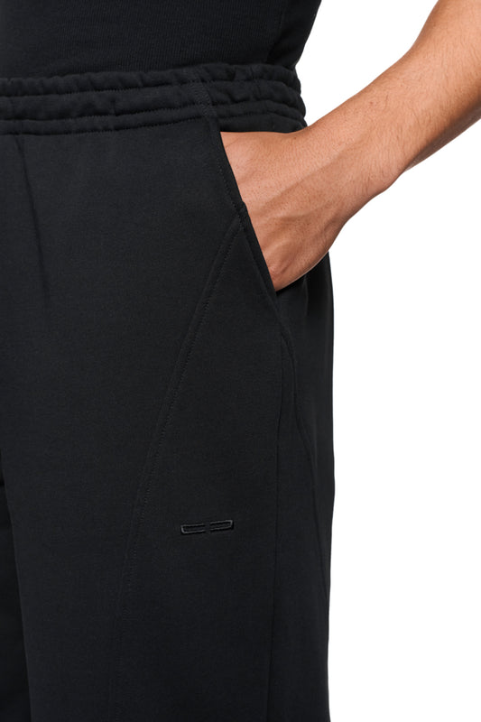 Hand in der Tasche einer schwarzen CC Core Sweatpants aus strapazierfähiger Mischfaser mit elastischem Bund und Rippbündchen, betont durch elegante Teilungsnähte.