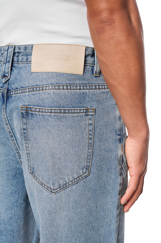 Person trägt CC Core Denim Pants Blue mit robustem Denim, OLAKALA PU-Patch am Bund, lockerer Passform und 5-Pocket-Style.