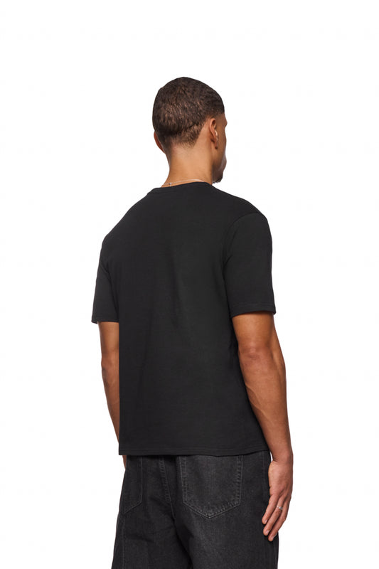 Mann trägt CC Core T-Shirt Black mit Ripp-Kragen und gesticktem OLAKALA Icon auf der Brust, reguläre Passform, unisex.