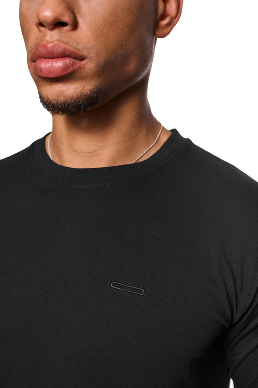 Nahaufnahme eines Mannes, der das CC Core T-Shirt Black mit gesticktem OLAKALA-Icon auf der Brust trägt, unisex und mit Ripp-Kragen.