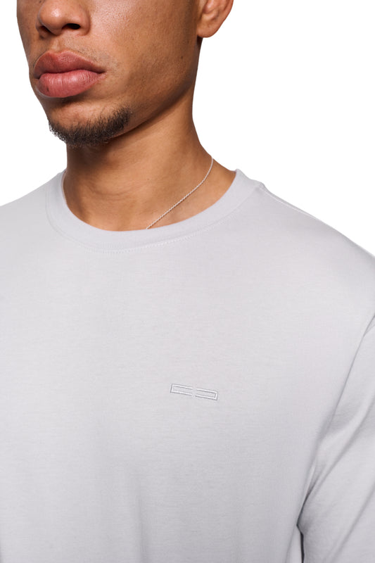 Mann trägt CC Core T-Shirt Grau mit Ripp-Kragen und gesticktem OLAKALA-Icon auf der Brust, unisex und reguläre Passform.