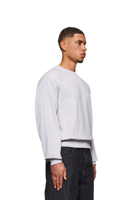 Mann trägt CC Core Sweater Gray mit Rippbündchen und versetzten Nähten für Komfort. Langlebige Mischfaser, reguläre Passform, unisex Design.