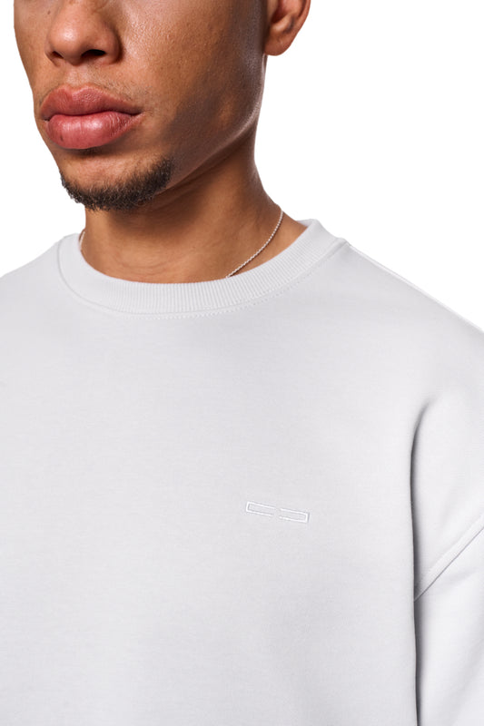 Nahaufnahme eines Mannes, der den CC Core Sweater Gray trägt, mit Rippbündchen und regulärer Passform, zeigt Komfort- und Langlebigkeitsmerkmale des Unisex-Designs.