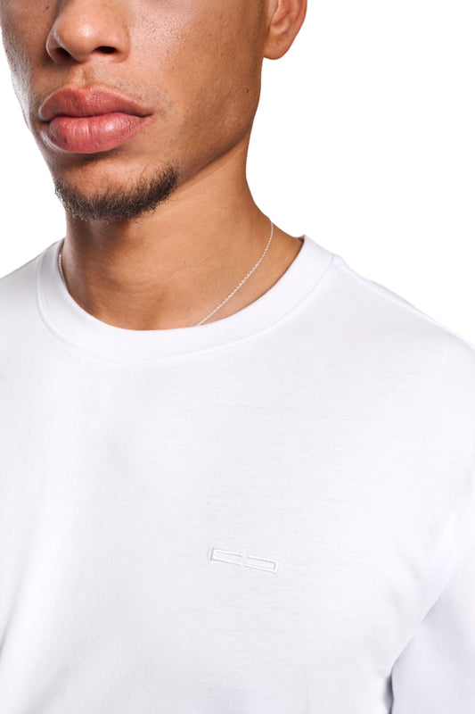 Nahaufnahme eines Mannes, der das CC Core T-Shirt White mit gesticktem OLAKALA-Icon auf der Brust trägt, zeigt Kragen und reguläre Passform.