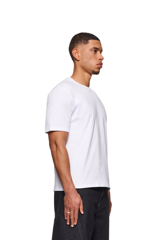 Mann im CC Core T-Shirt Weiß mit gesticktem OLAKALA-Icon auf der Brust, zeigt den Ripp-Kragen und die reguläre Passform. Unisex-Design.