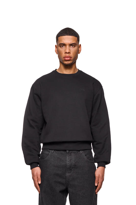 Man wears CC Core Sweater Black with ribbed cuffs and tucked seams for comfort. Unisex, regular fit, durable.