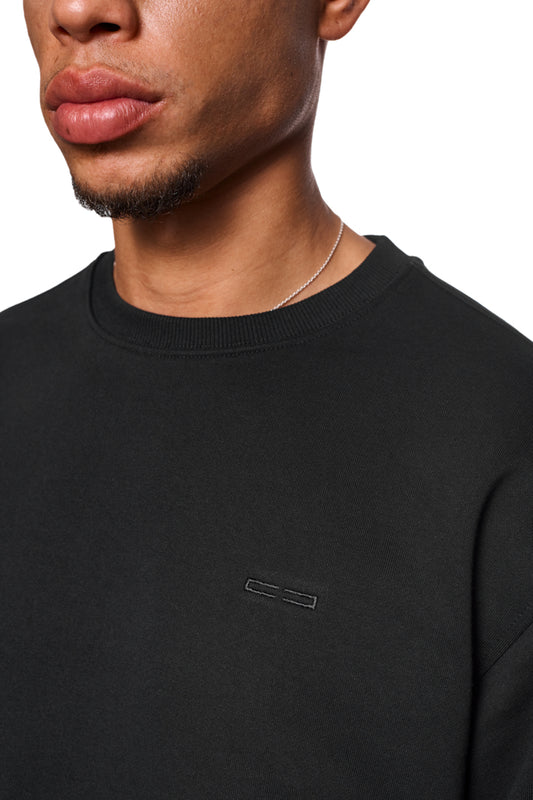 Nahaufnahme eines Mannes, der den CC Core Sweater Black trägt, mit Rippbündchen und strapazierfähiger Mischfaser für Langlebigkeit und Tragekomfort.