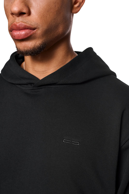 Nahaufnahme eines Mannes, der den CC Core Hoodie Black trägt, mit Kängurutasche und Rippbündchen, betont die reguläre Passform und den Tragekomfort.