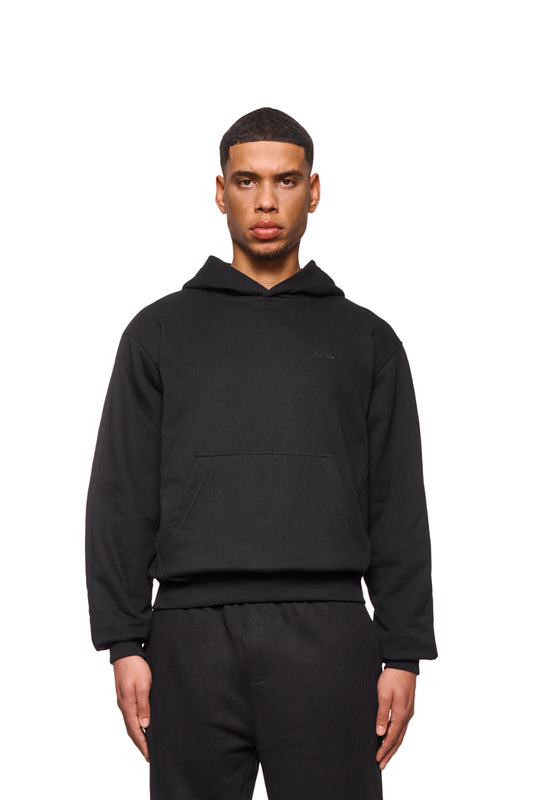 Mann trägt CC Core Hoodie Black mit Kängurutasche und Rippbündchen, reguläre Passform.