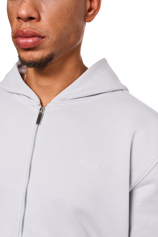 Nahaufnahme eines Mannes, der den CC Core Zip Hoodie Gray trägt, mit Reißverschluss und Kängurutasche, betont Langlebigkeit und Komfort durch strapazierfähige Mischfaser und verlegte Nähte.