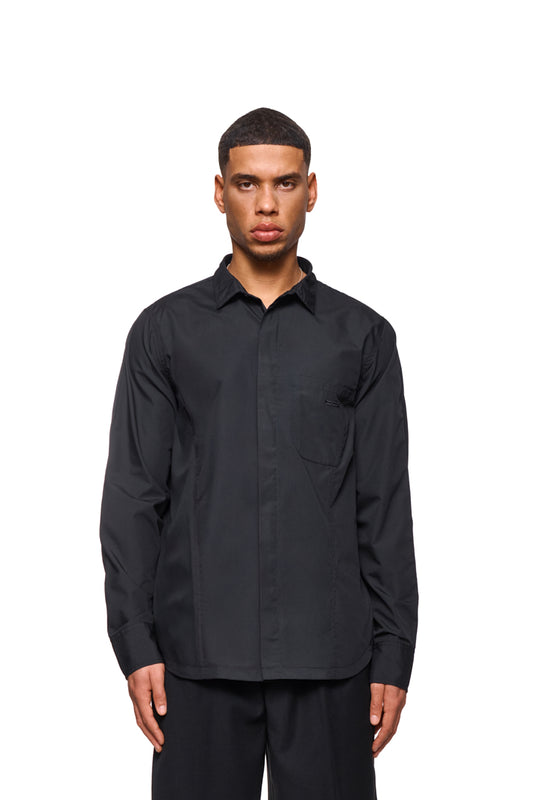 Mann trägt das CC Core Button Shirt Black mit verdeckter Knopfleiste und Brusttasche, betont durch verlegte Nähte für Komfort.