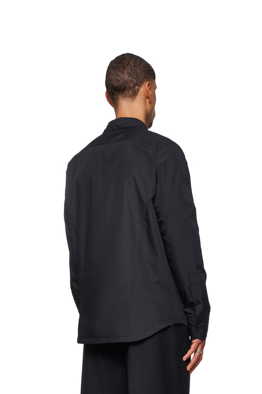 Mann trägt das CC Core Button Shirt Black, mit verdeckter Knopfleiste und Brusttasche. Langlebige Mischfaser und verstärkter Kragen für Komfort.
