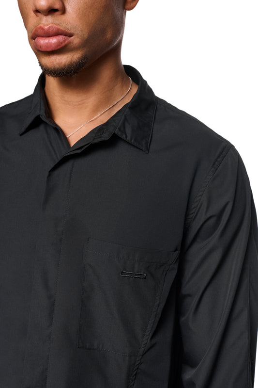 Mann trägt CC Core Button Shirt Black mit Brusttasche und verdeckter Knopfleiste, verlegte Nähte für Komfort, unisex Design.