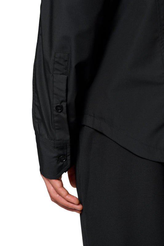 Nahaufnahme einer Hand, die den Ärmel des CC Core Button Shirt Black hält, mit Brusttasche und verdeckter Knopfleiste für Komfort und Langlebigkeit.