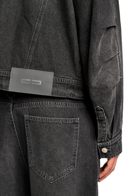 Nahaufnahme einer Hand, die eine Tasche des 0asis Denim Overshirt Black berührt, mit geprägtem OLAKALA-Patch und Knopfleiste, geeignet für kühlere Sommertage.