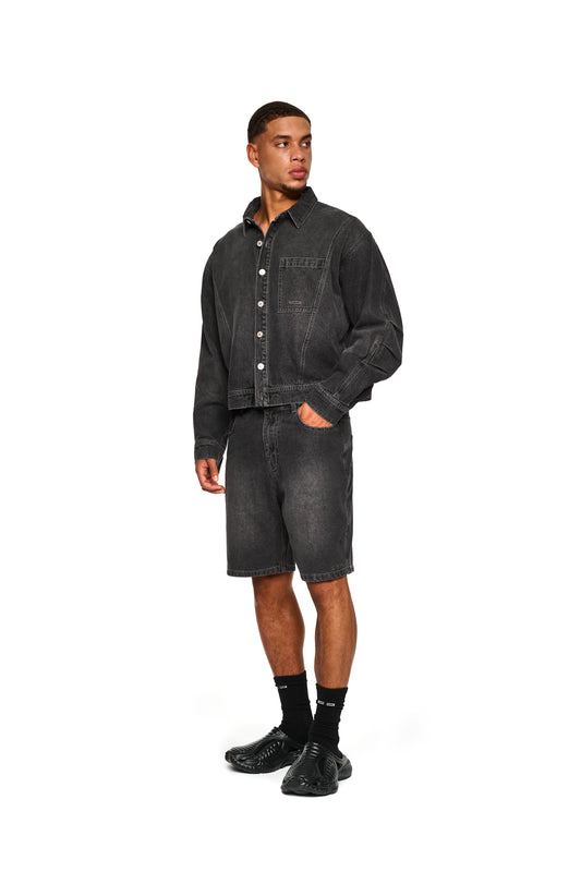 Mann trägt OLAKALA 0asis Denim Overshirt Black mit Knopfleiste, Brusttaschen und geprägtem Patch auf der Rückseite, passend für kühlere Sommertage.