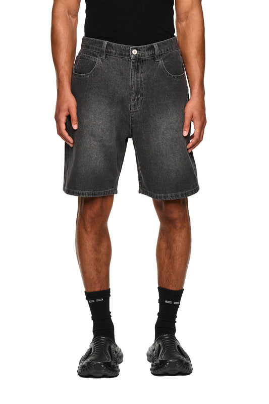Nahaufnahme der 0asis Denim Shorts Black mit geprägtem OLAKALA Patch und auffälliger Tasche, getragen mit schwarzen Schuhen und Socken, zeigt reguläre Passform und Logo-Stickerei.