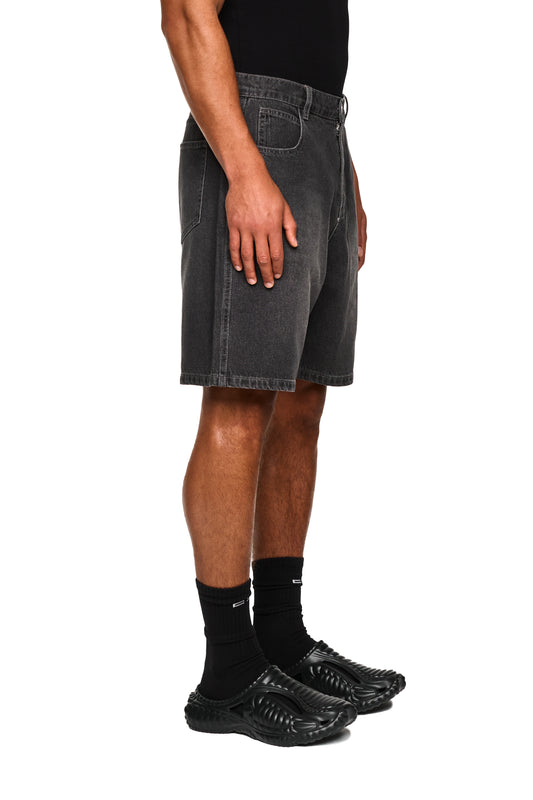 Nahaufnahme der OLAKALA 0asis Denim Shorts Black mit versetzter Passe, aufgesetzter Tasche und geprägtem OLAKALA Patch, getragen von einer Person.