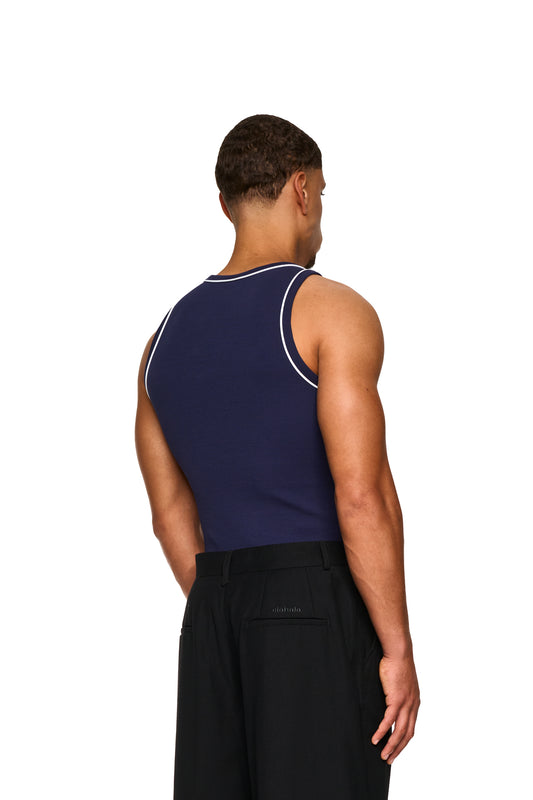 Mann im Contrast Tanktop Navy Blue mit gesticktem OLAKALA Icon auf der Brust, zeigt elastischen Ripp-Stoff und kontrastfarbene Paspellierungen.