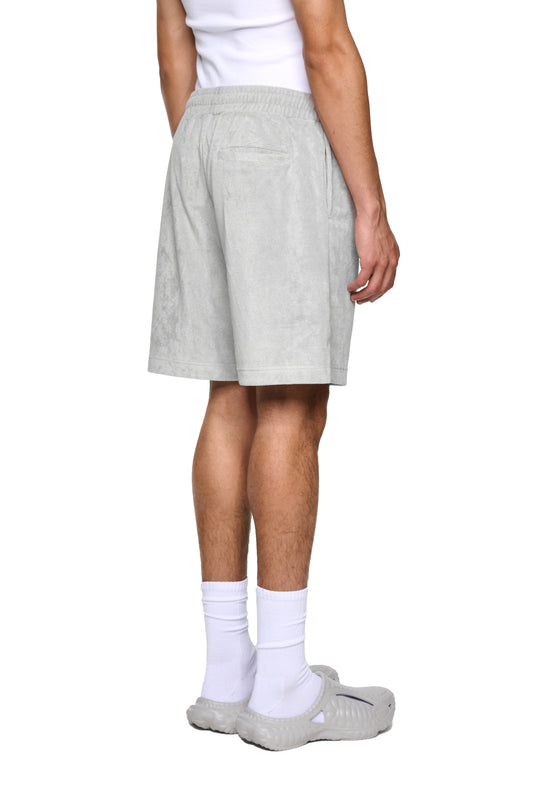 Hand mit Fokus auf graue Terry Shorts aus Frottee, elastischer Bund mit Kordelzug, Rückentaschen und Logo-Stickerei, präsentiert im OLAKALA Onlineshop.