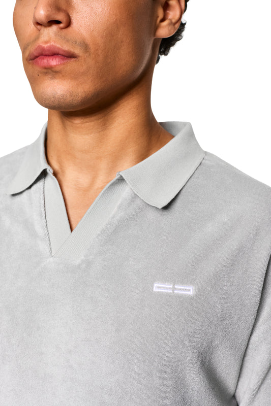 Nahaufnahme eines Gesichts mit Fokus auf einem grauen Terry Polo aus weichem Frotteematerial mit Logo-Stickerei auf der linken Brust.